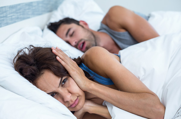 A woman covering her ears as husband with sleep apnea snores at Singing River Dentistry in Florence, AL