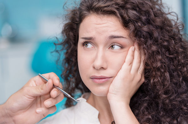 Woman holding cheek before a tooth extraction at Singing River Dentistry in Florence, AL 